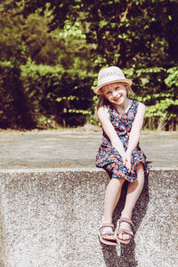 Portrait of cute smiling girl wearing hat sitting on retaining wall