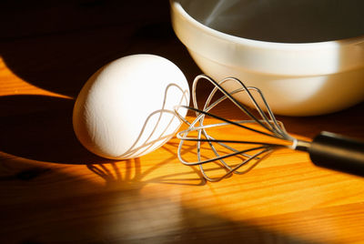 Close-up of egg and wire whisk on table