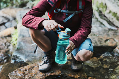 Woman taking pure water to bottle from mountain stream during trekking in mountains