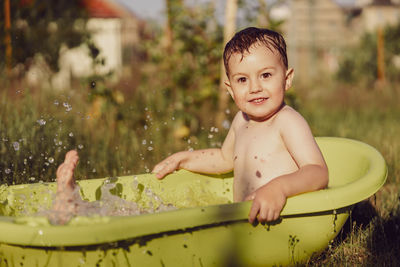 Cute little boy bathing in tub outdoors in garden. happy child is splashing, playing with water 
