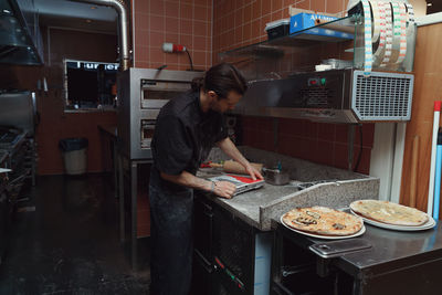 Side view of man preparing pizza in kitchen