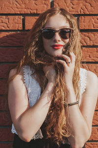 Portrait of a young redhead woman leaning against brick wall