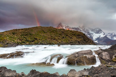 Scenic view of river with rainbow over mountain against sky