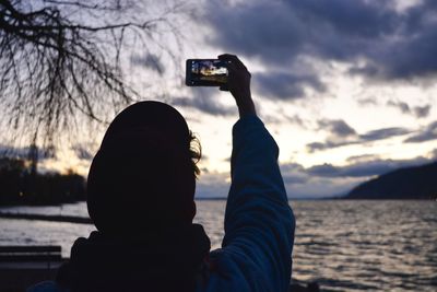 Woman photographing at beach against sky