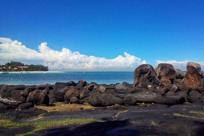 Rocks by sea against blue sky