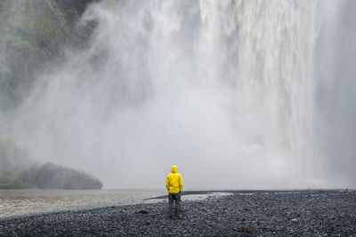 Rear view of woman standing against waterfall