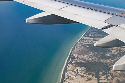 Aerial view of airplane wing over landscape against blue sky