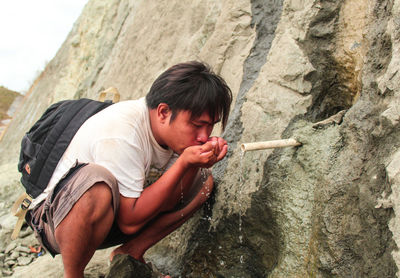 An asian man drinking from a flowing spring