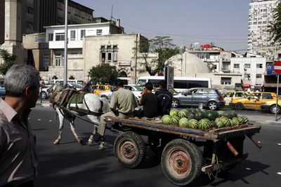 Man looking at people carrying watermelons on horse cart at street