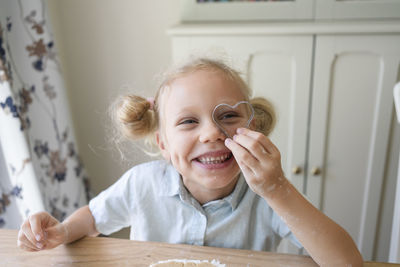 Happy girl looking through heart shaped cookie cutter