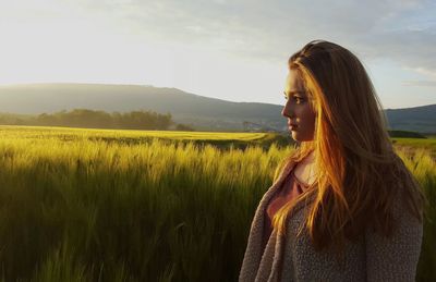 Young woman standing on field against sky