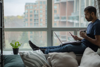 Man using mobile phone while sitting on window