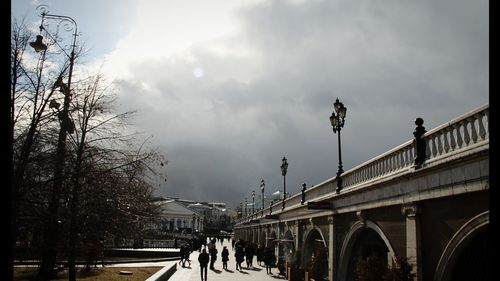 People on bridge in city against sky