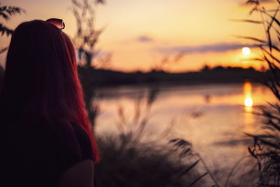 Rear view of woman looking at lake against sky during sunset
