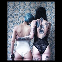 Tattooed women in swimwear standing against patterned wall