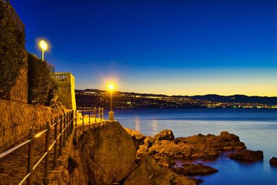 Illuminated rocks by sea against clear blue sky at night