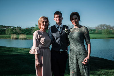 Portrait of friends standing by lake against sky