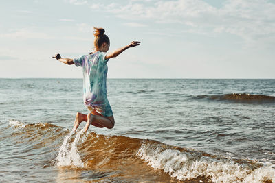 Girl enjoying sea jumping over waves spending a free time over sea on a beach at sunset