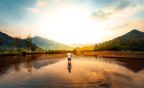 Man on lake against sky during sunset