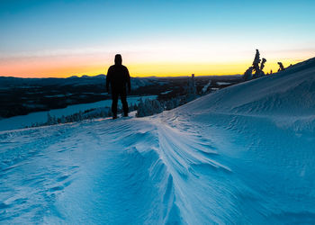 Silhouette man standing on snow covered land against sky during sunset