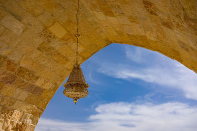 Low angle view of decoration hanging on historic arch against blue sky