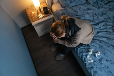 Young girl sitting on the bed and holding her head. woman feeling sick, suffer from cold and flu. 