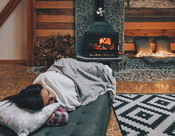 Woman sleeping on couch by fireplace in cozy warm cabin.