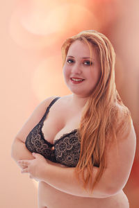 Portrait of young woman in bra standing against colored background