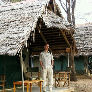 Young man standing below thatched roof hut