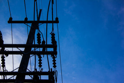 Low angle view of silhouette electricity pylon against blue sky