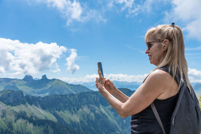 Side view of woman with arms raised standing against mountain