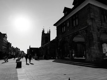 People walking on street amidst buildings in city against sky