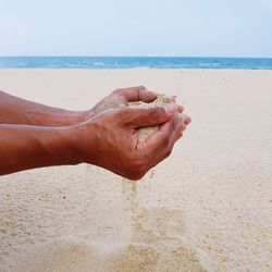 Close-up of hand holding sand at beach against clear sky