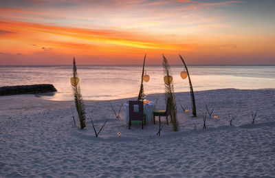 Dinner place setting at beach against sky during sunset