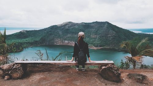 Full length of woman looking at view while sitting by lake against sky