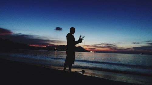Silhouette man holding remote control of drone at beach during sunset