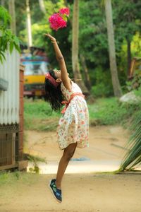 Full length of happy girl throwing flowers while jumping in park