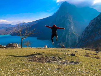 Rear view of man jumping on mountain against sky