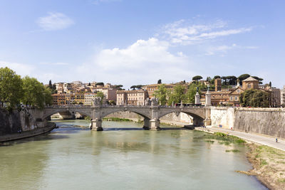 Arch bridge over river by buildings against sky