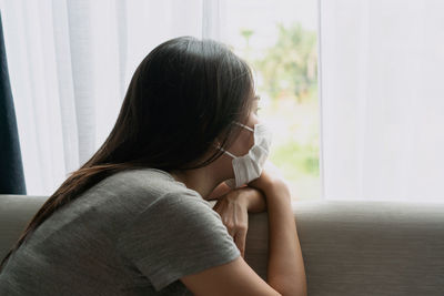 Side view of young woman looking away while sitting on sofa at home