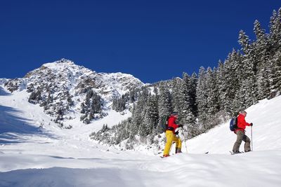 People skiing on snowcapped mountain against clear blue sky