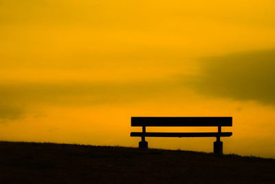 Empty bench on silhouette field against sky during sunset