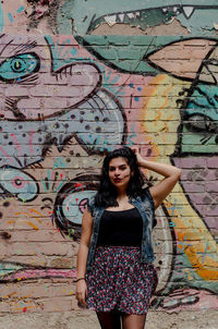 Portrait of young woman standing against graffiti wall