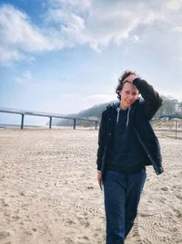 Portrait of young woman standing at beach against sky