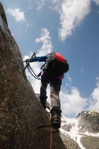 Low angle view of boy climbing on mountain against sky