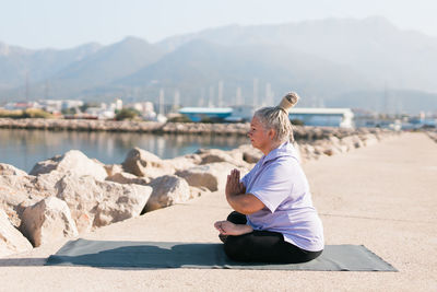 Side view of woman sitting on rock by lake