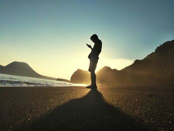 Silhouette man standing on beach against sky