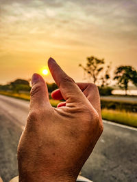 Close-up of hand against sky during sunset