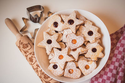 Top view of the bowl of linzer cookies against a table cloth and a dough roller