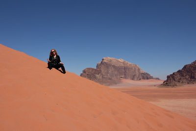 Man with umbrella on desert against clear sky